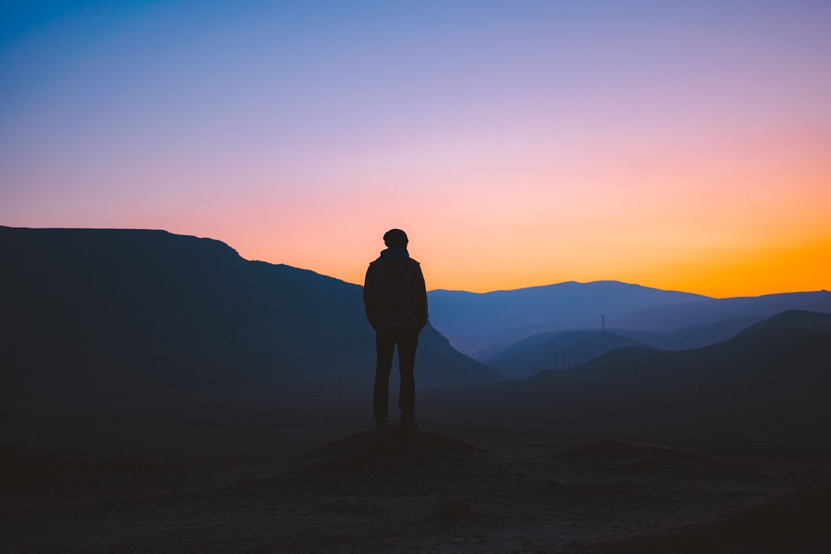 Silhouette of a person standing on a mountain summit at sunset, evoking leadership and courage